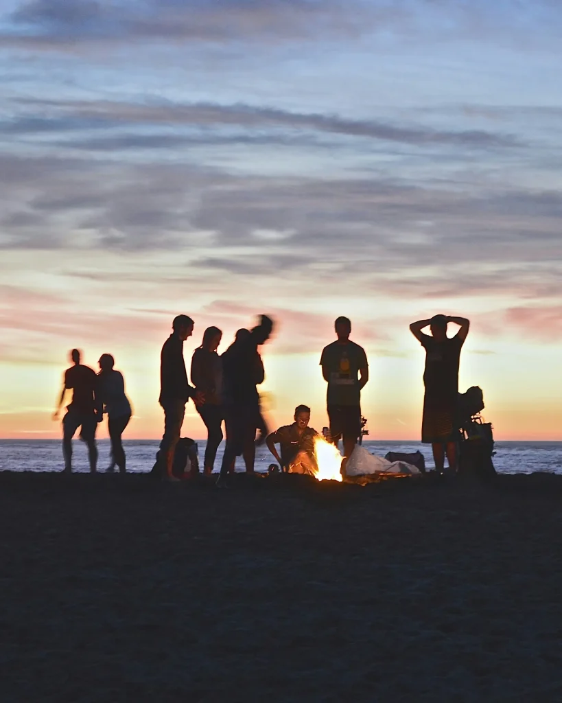elever rundt bål på strand etter solnedgang